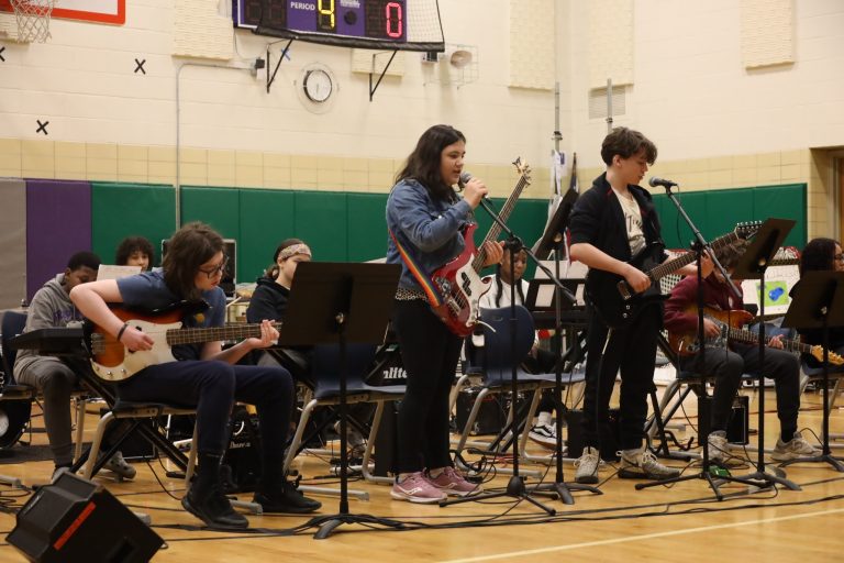 Nine students performing in a band, featuring a singer, multiple guitarists, pianists, bassists, and drummers.